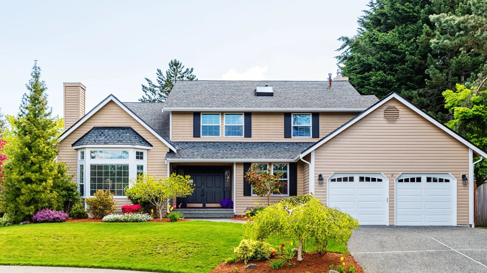 Beige two-story home with black shutters and a gray asphalt shingle roof