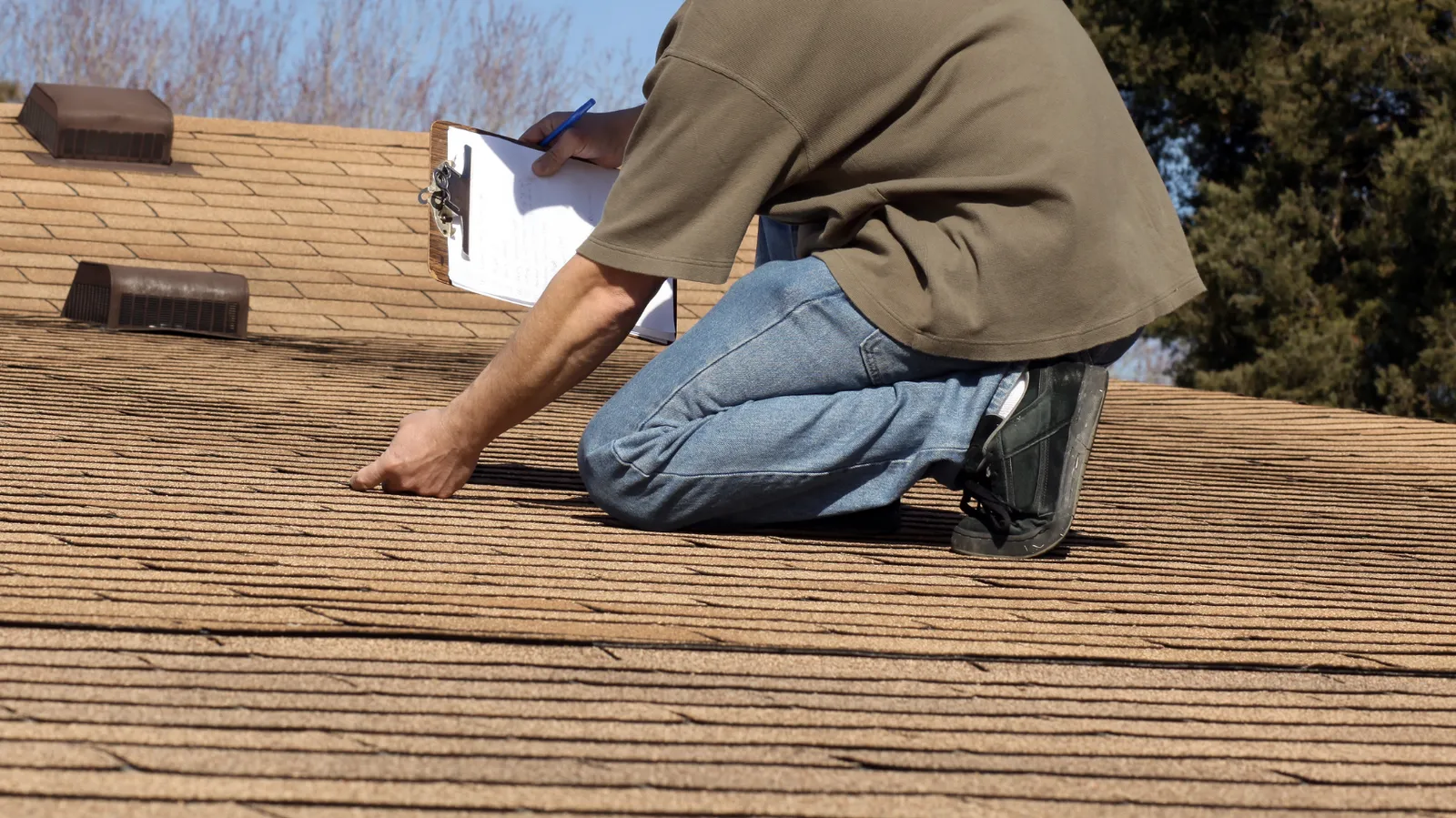 Near roof vents an inspector holding a clipboard checks shingles