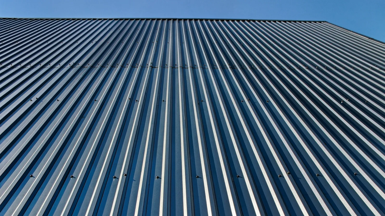 Clear sky behind ribbed metal cladding seen looking upward